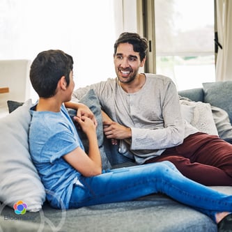 A father and his tween son sit comfortably on a sofa, having a calm and connected conversation. (1)